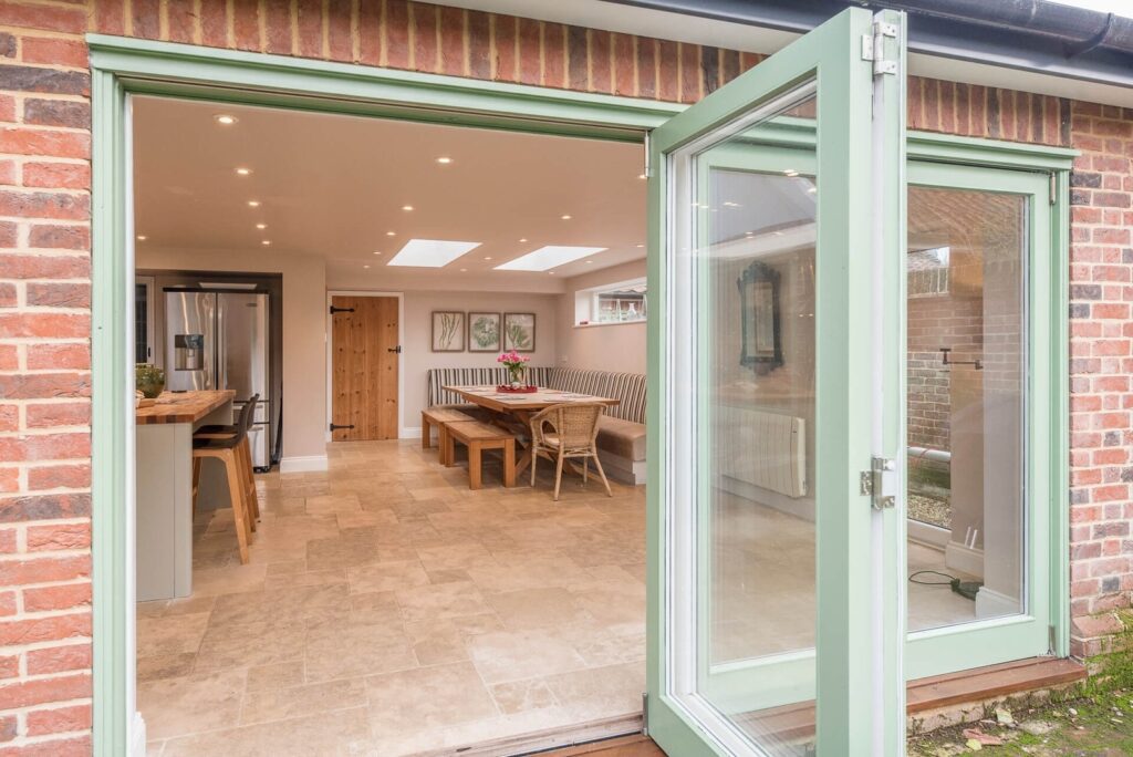 Large glass doors open to reveal a spacious open-plan kitchen and dining area in light wood