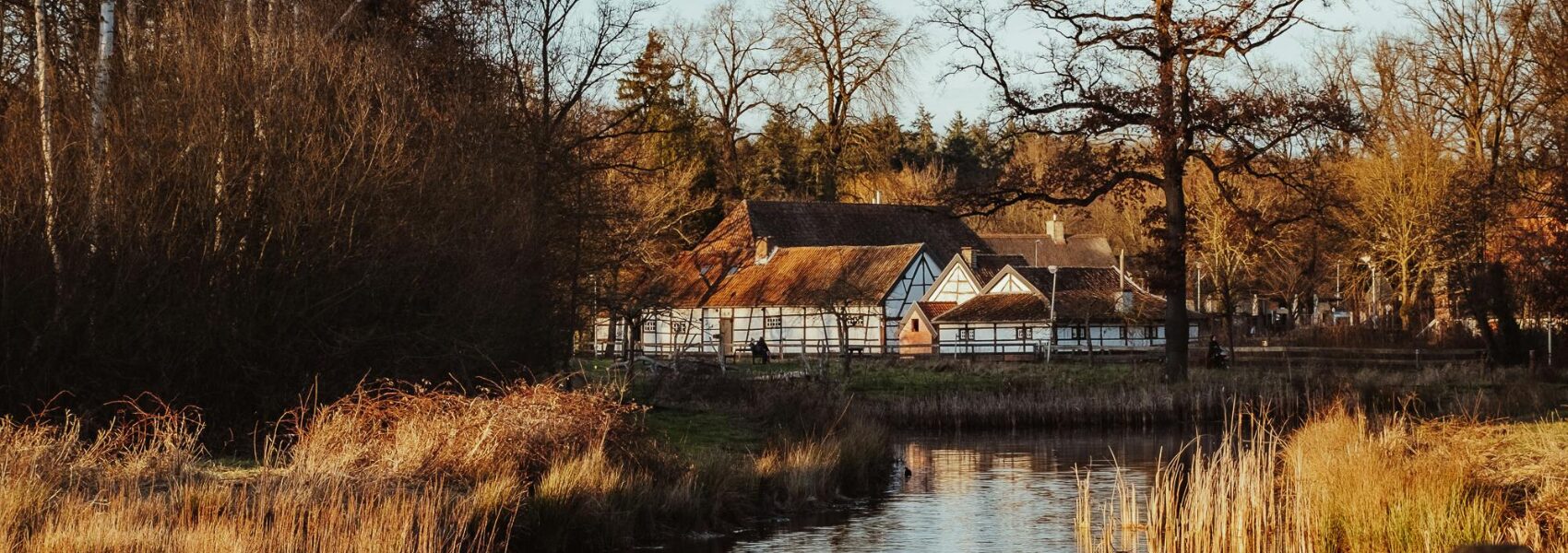 A cluster of beautiful old white and brown timber houses set amongst trees on the bank of a river in autumn