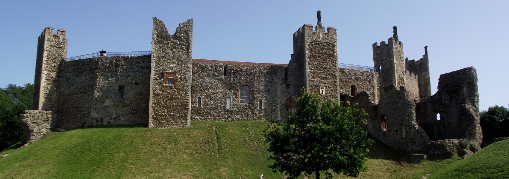 The side of a large stone brick castle on top of a sloping green grassy hill