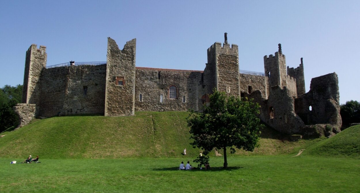 The side of a large stone brick castle on top of a sloping green grassy hill